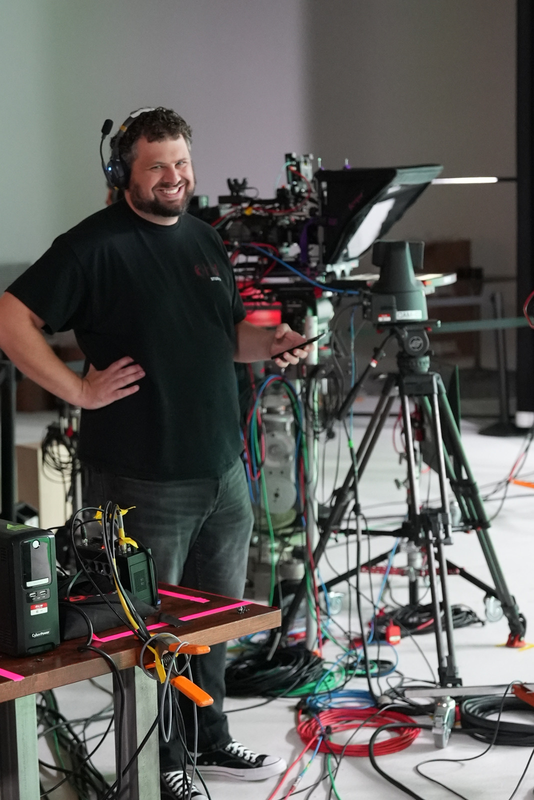 Alex Nowak on set beside a camera and teleprompter